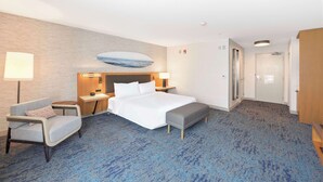 Ein Hotelzimmer mit einem großen Bett, einem Nachttisch mit Lampe, einem Sessel und einem kleinen Tisch.