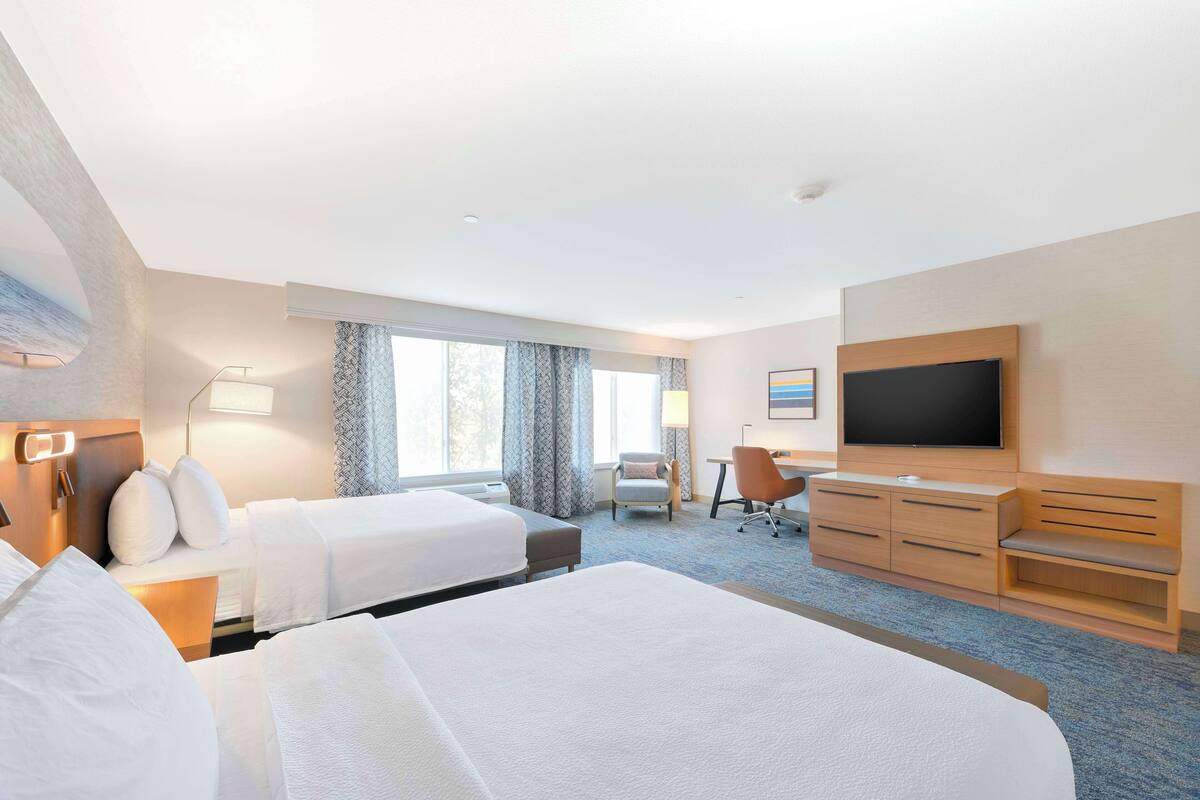 A hotel room with two beds, a desk, a chair, a TV, and a large window.