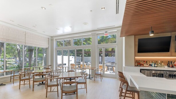 Ein modernes Restaurant mit Barbereich, großen Fenstern und einer durch die Glaswände einsehbaren Küche.
