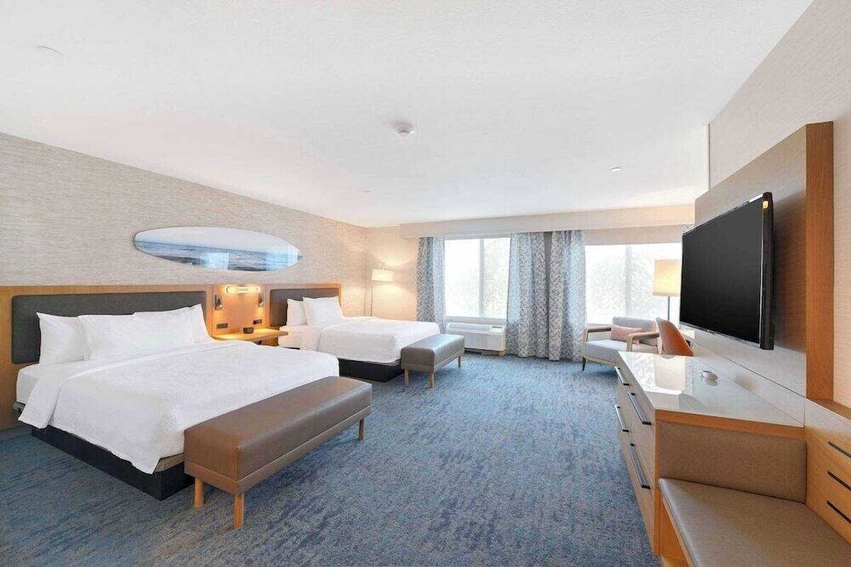 A hotel room with two beds, a desk, a flat-screen TV, and a large window.