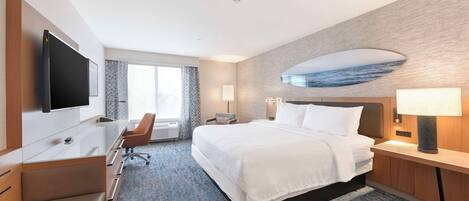 Habitación de hotel con cama, escritorio, televisor, ventana y una obra de arte en la pared.