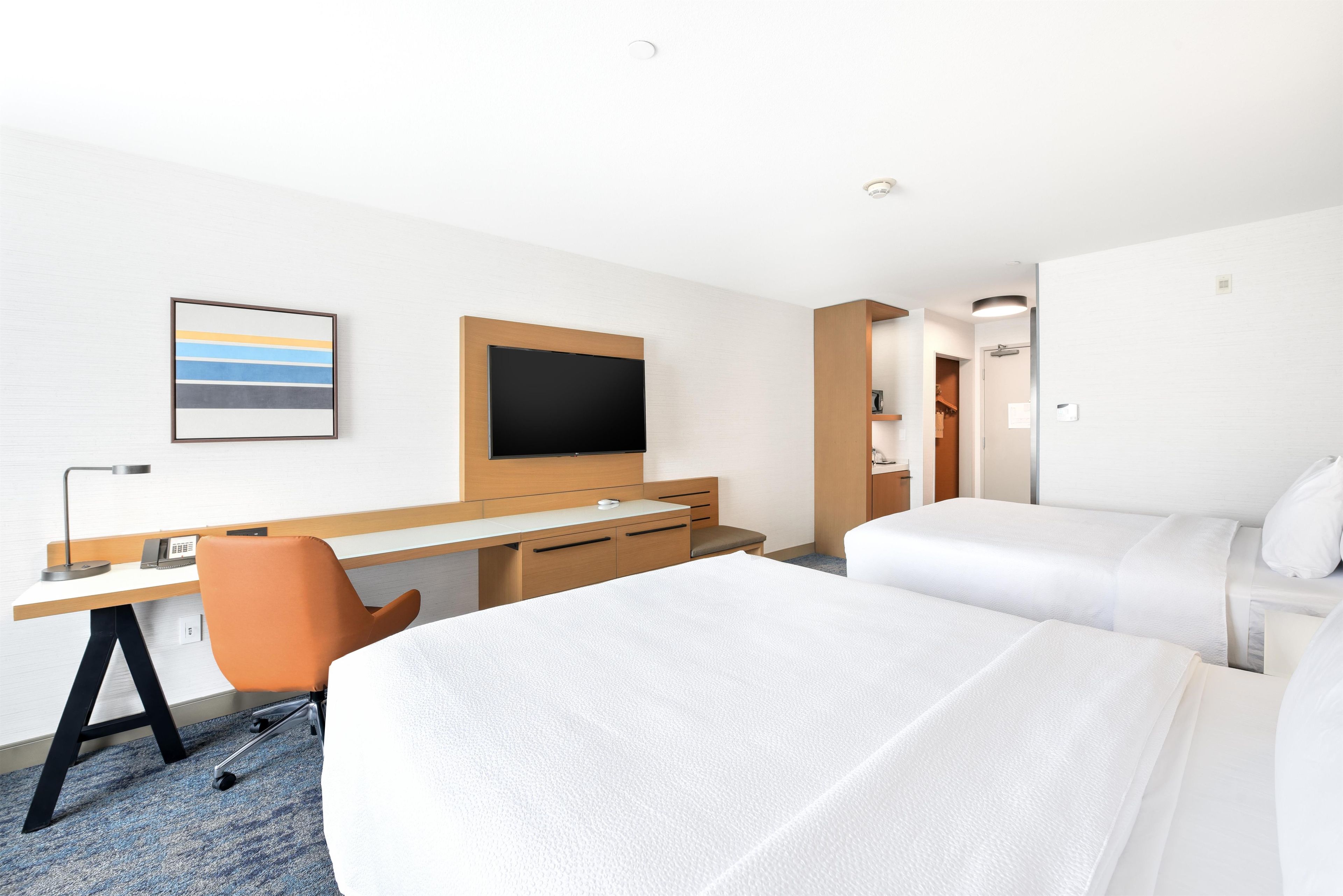A hotel room with a bed, a desk, a chair, a television, and a framed picture on the wall.