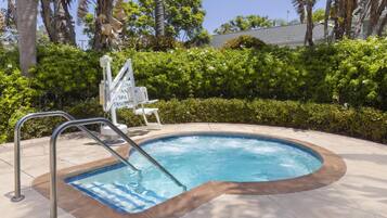 A swimming pool with a metal ladder, surrounded by a tiled deck and lush greenery.