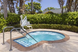 A swimming pool with a metal ladder, surrounded by a tiled deck and lush greenery.