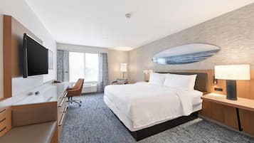 A hotel room with a bed, desk, chair, TV, and a large window.