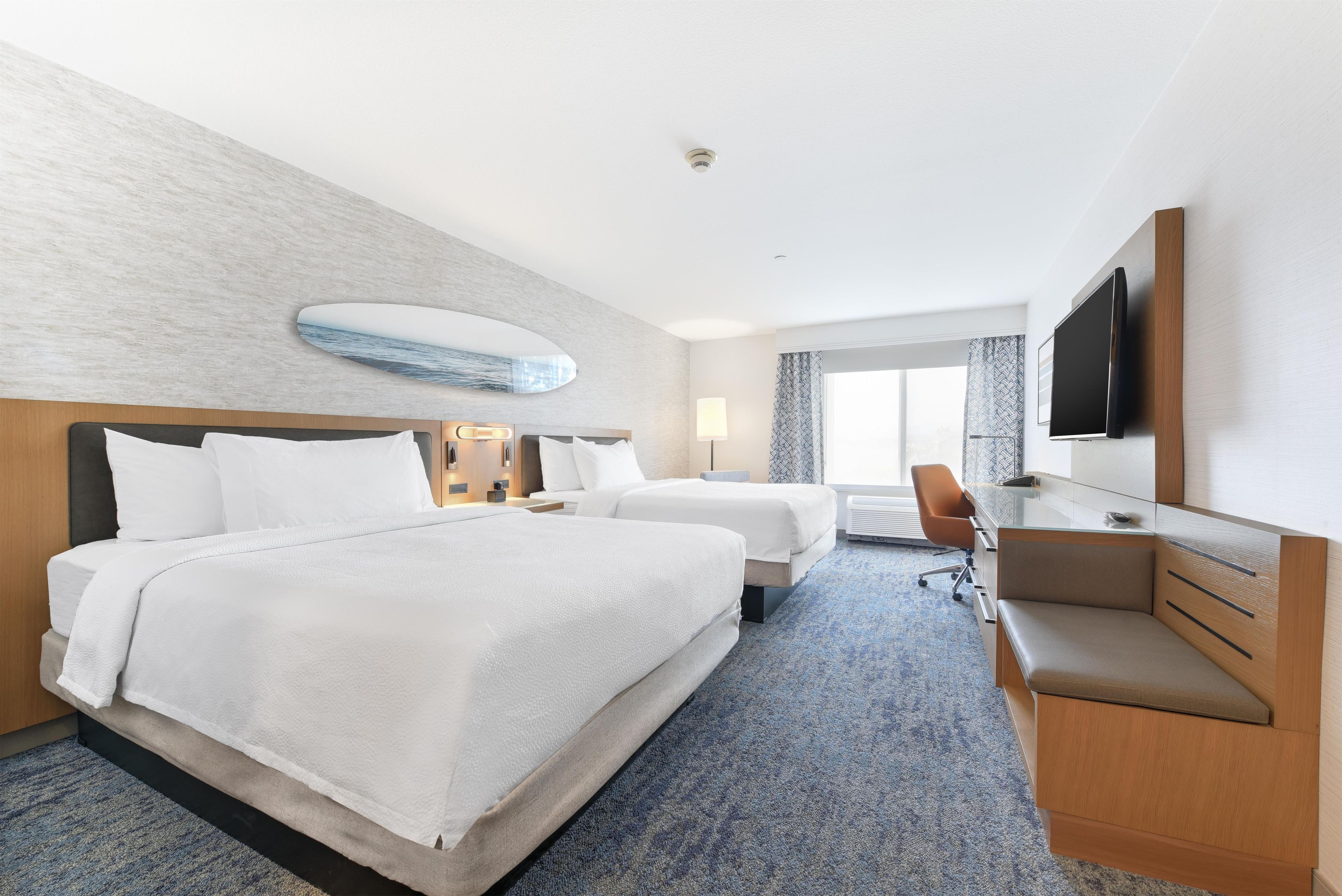 A hotel room with two beds, a desk, a chair, and a television.