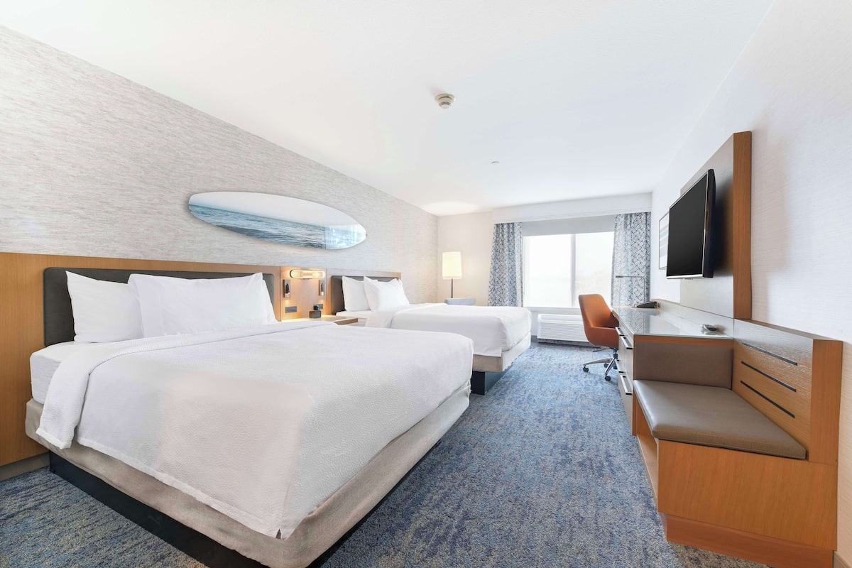 A hotel room with two beds, a desk, a TV, and a large window.