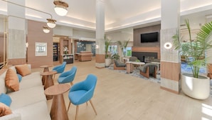 Eine geräumige Lobby mit einer Rezeption, einer Sitzecke mit blauen Stühlen, einem an der Wand montierten Fernseher und einer großen Topfpflanze.