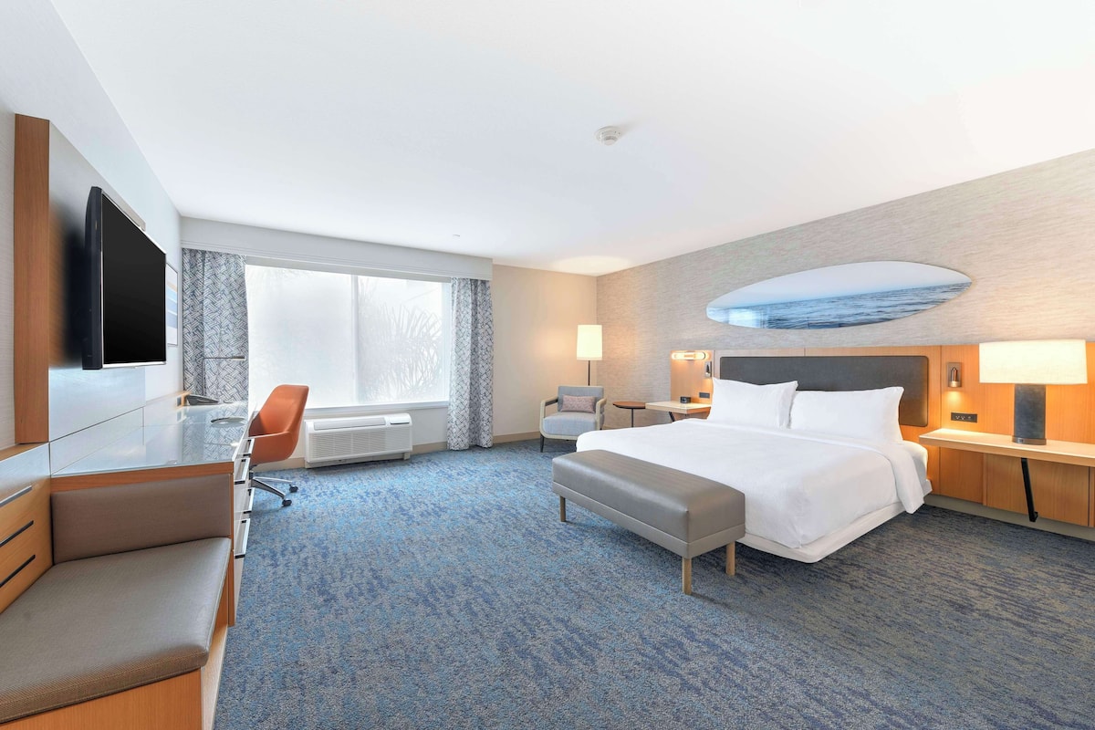 A hotel room with a large bed, a desk, a chair, a TV, and a view of the outdoors.
