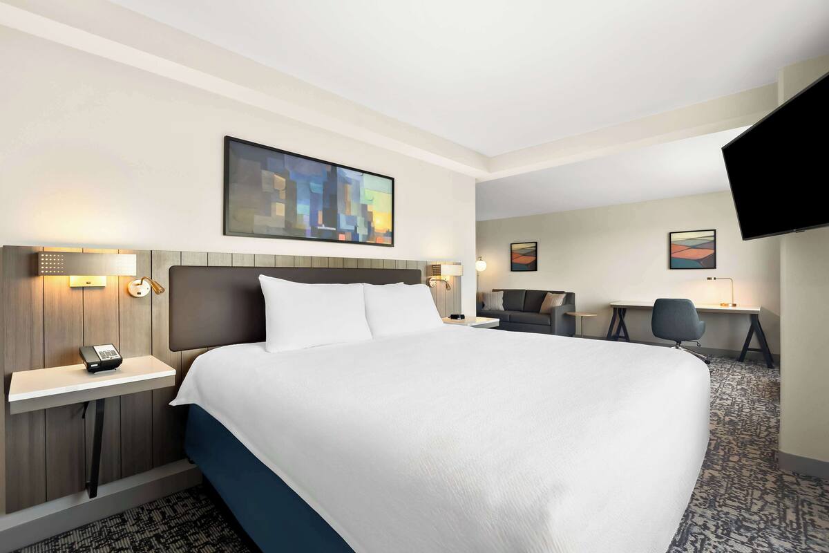 A hotel room with a large bed, a desk, a chair, and a flat-screen TV.
