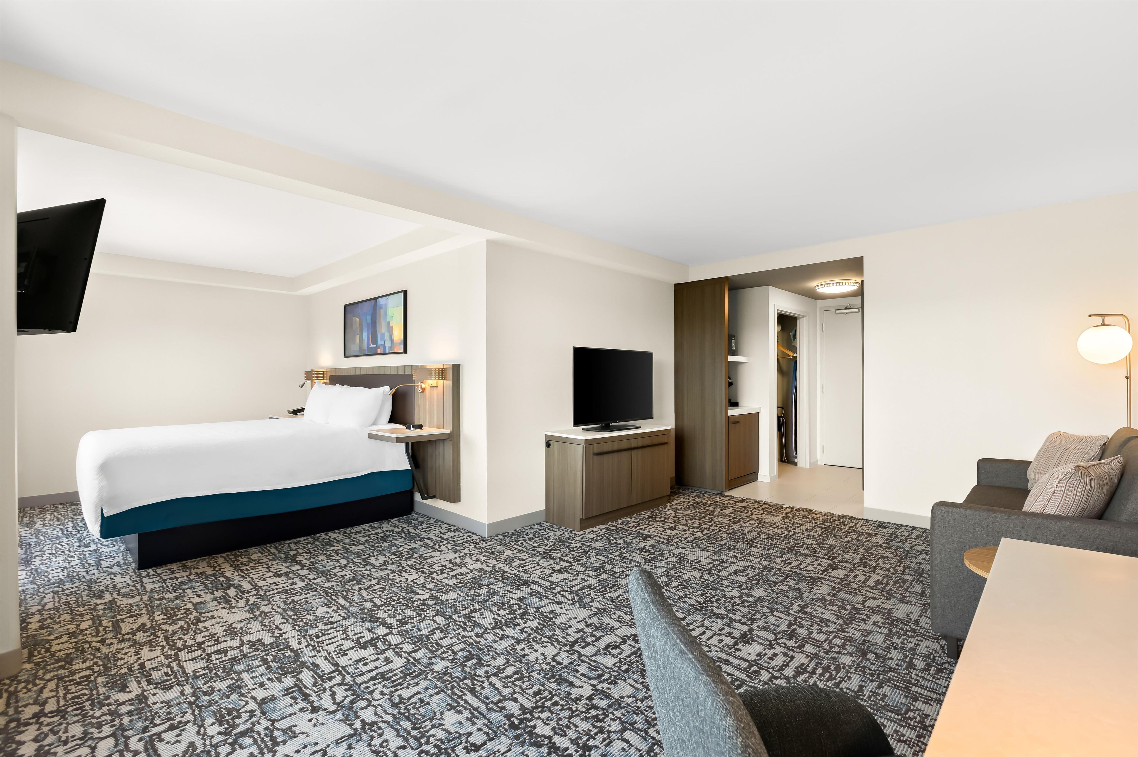 A hotel room with a bed, a desk, a television, a sofa, and a patterned carpet.