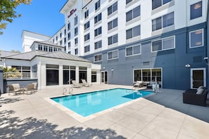 A hotel with a swimming pool, outdoor seating, and a modern building facade.