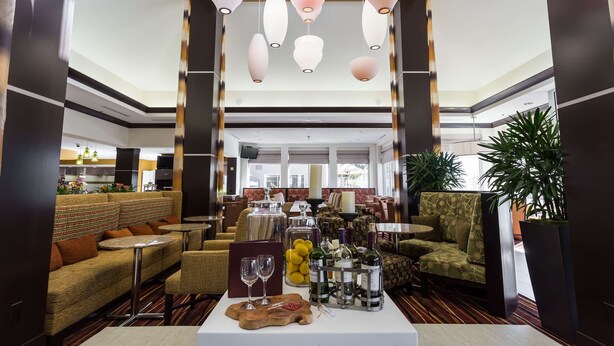 A spacious lobby with seating areas, a bar, and a dining area. - Hilton Garden Inn San Mateo (San Mateo)