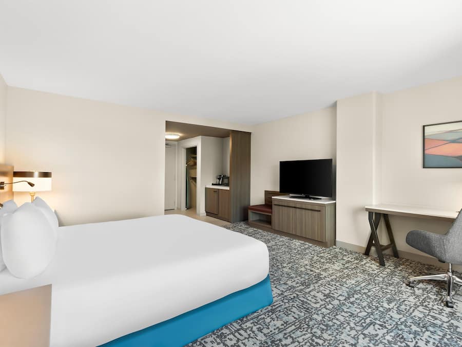A hotel room with a bed, a desk, a chair, a television, and a bathroom visible through an open door.