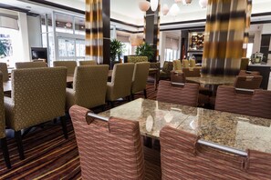 A hotel dining area with patterned chairs, a marble table, and a view of the kitchen in the background. - Hilton Garden Inn San Mateo (San Mateo)