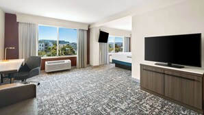 A hotel room with a large window, a flat-screen TV, a bed, a desk, and a chair. - Hilton Garden Inn San Mateo (San Mateo)