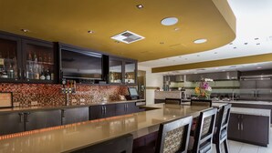 A modern kitchen with a central island, dark cabinetry, and a tiled backsplash. - Hilton Garden Inn San Mateo (San Mateo)