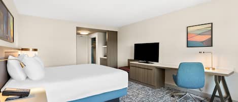 A hotel room with a bed, desk, chair, TV, and artwork.