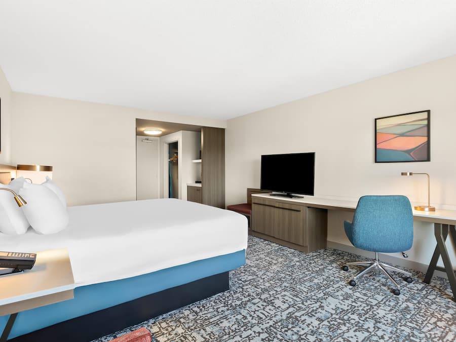 Habitación de hotel con cama, escritorio, silla, televisión y obras de arte.