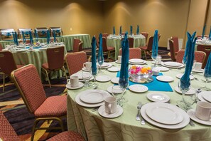 A banquet hall with round tables set for dining, featuring white plates, silverware, and blue napkins.