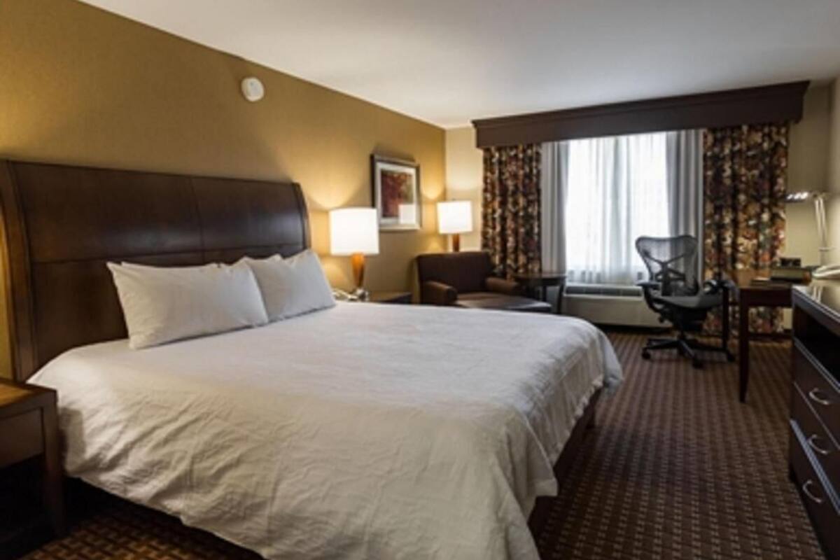 A hotel room with a large bed, a desk, a chair, and a window with curtains.