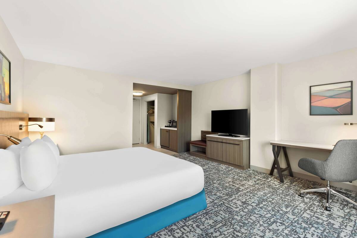 A hotel room with a bed, a desk, a chair, a television, and a bathroom visible through an open door.