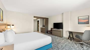 A hotel room with a bed, a desk, a chair, a television, and a bathroom visible through an open door.