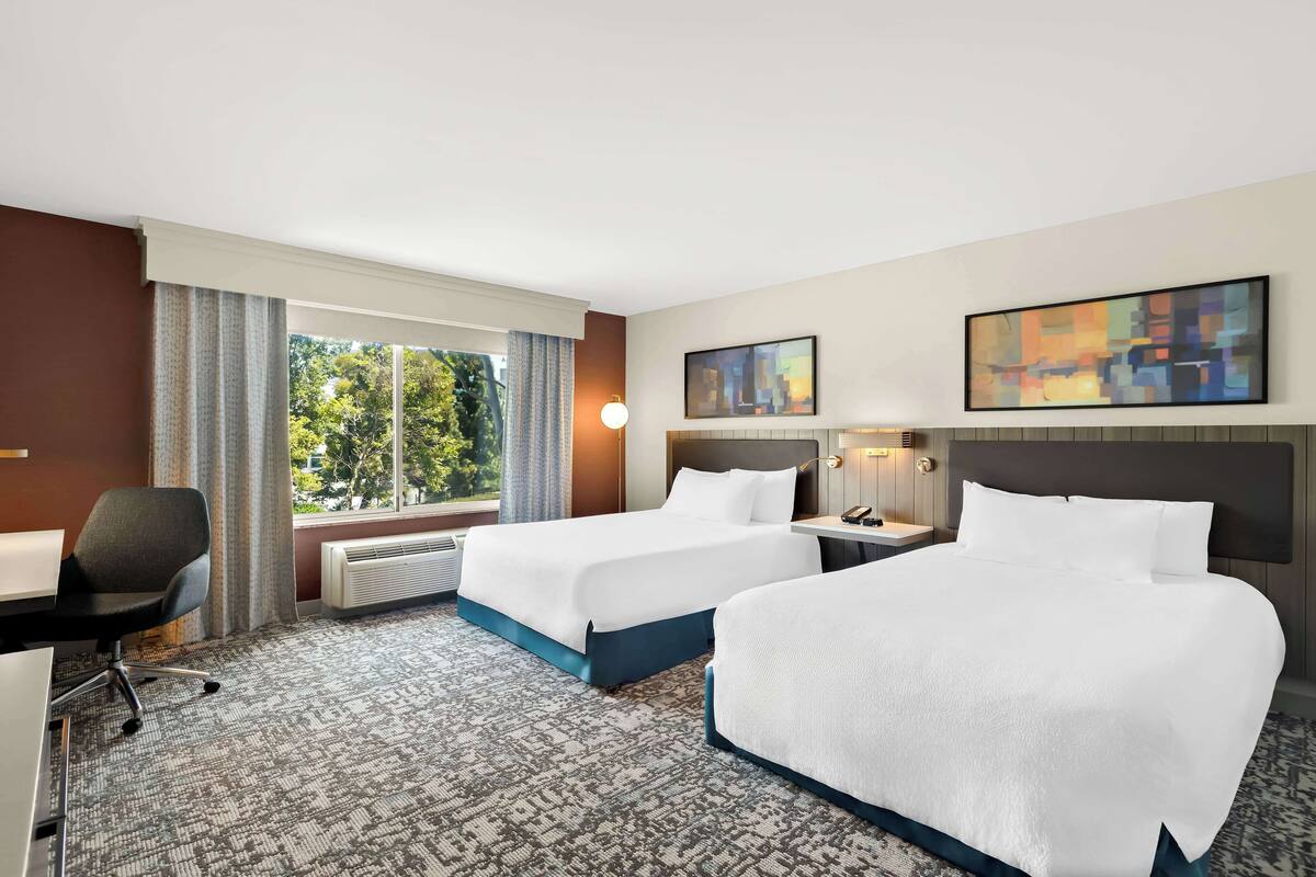 A hotel room with two beds, a desk, and a chair.