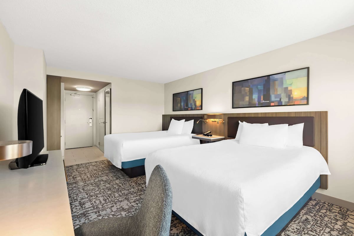 A hotel room with two beds, a desk with a flat-screen TV, a chair, and artwork on the walls.