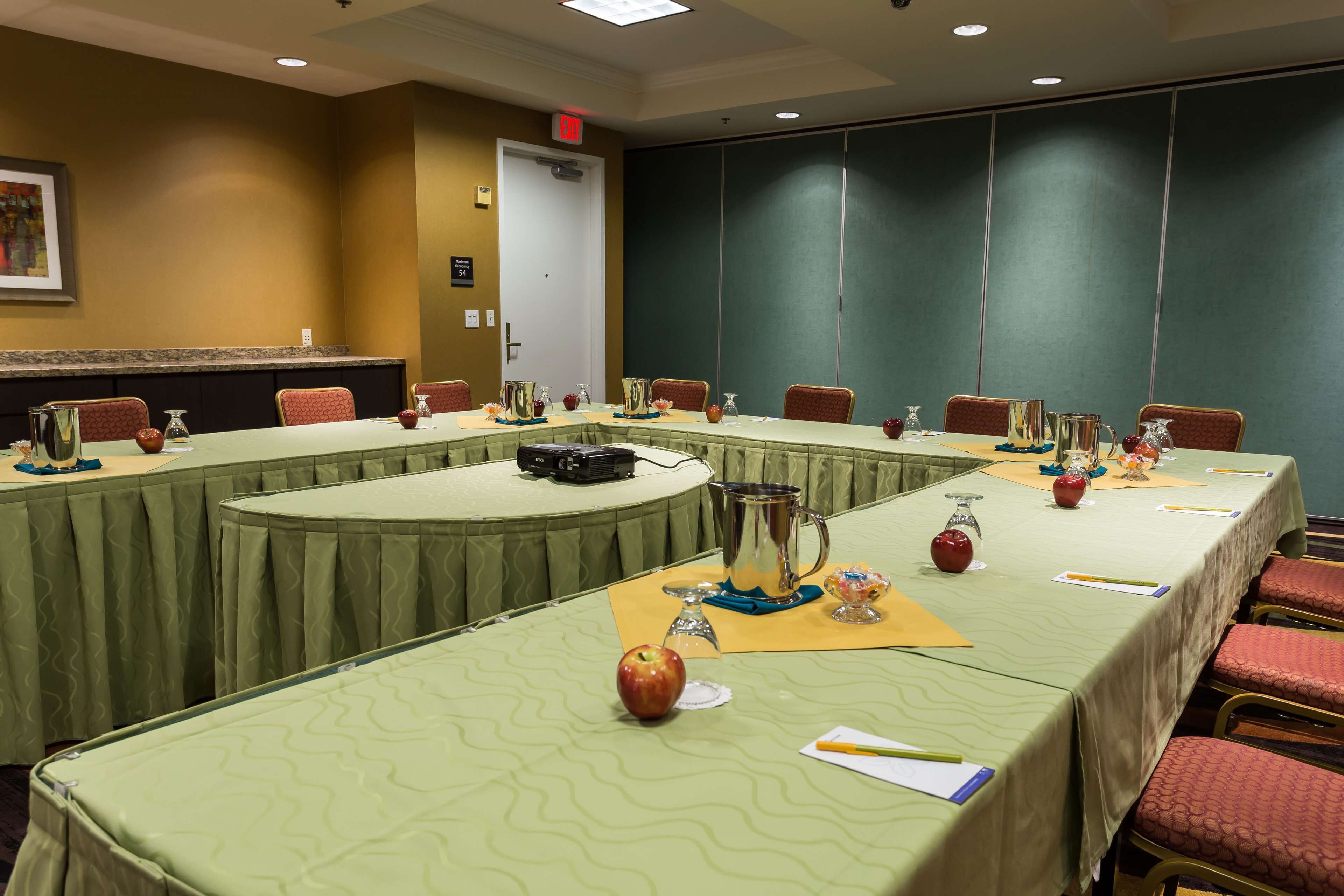 Un salón de conferencias con una larga mesa, sillas y diversos objetos como una cámara, manzanas y un micrófono.