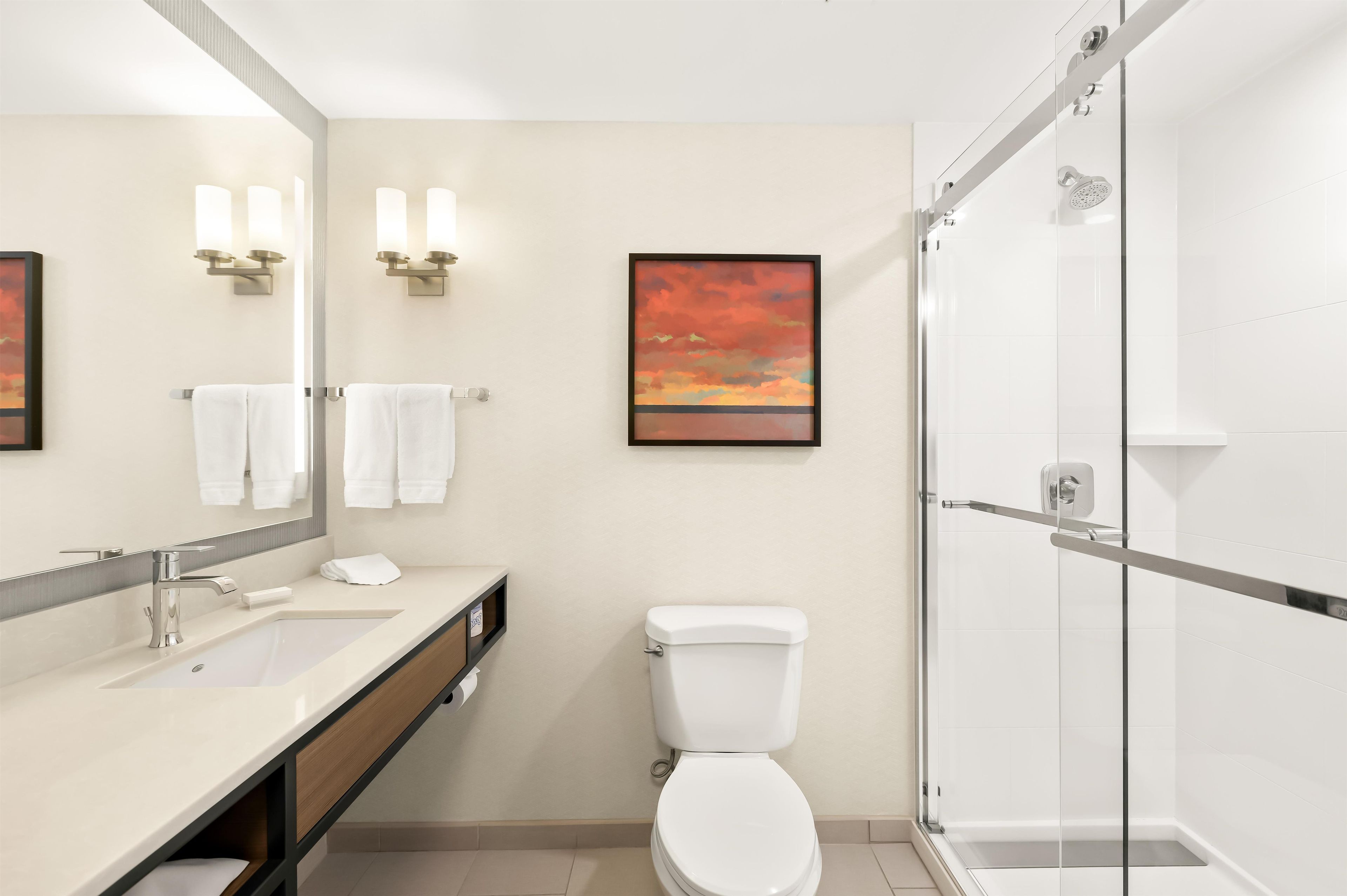 A modern bathroom with a glass shower enclosure, a toilet, a sink with a mirror, and wall-mounted lights.