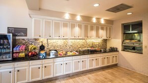 A kitchen with white cabinets, a tiled backsplash, and a counter with food items and a waffle maker.