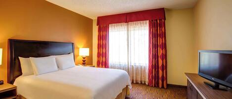 A hotel room with a large bed, a flat-screen TV, a nightstand, and a window with curtains.