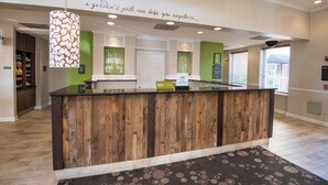 A reception desk with a wooden finish, a green accent wall, and a sign that reads "a garden's path can take you anywhere."