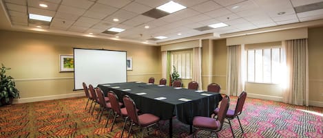 A conference room with a long table, chairs, a projector screen, and a patterned carpet.