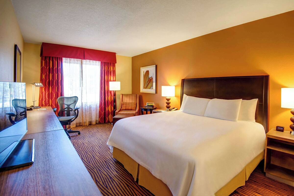 Ein Hotelzimmer mit einem großen Bett, einem Schreibtisch mit einem Laptop, einem Stuhl und einem Fernseher.