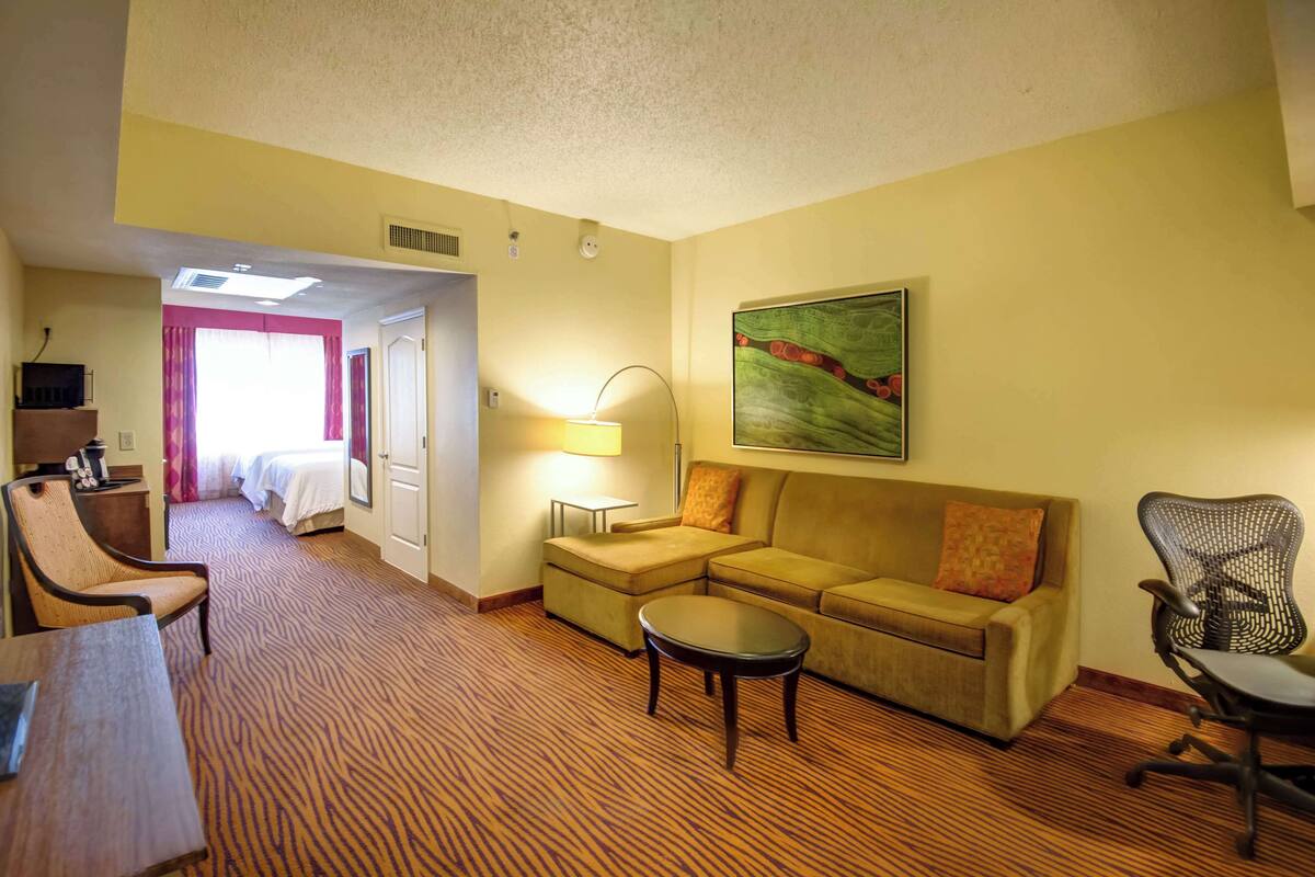 Ein Hotelzimmer mit Bett, einer Sitzecke, einem Schreibtisch, einer Lampe, einem Gemälde und einem Sessel.