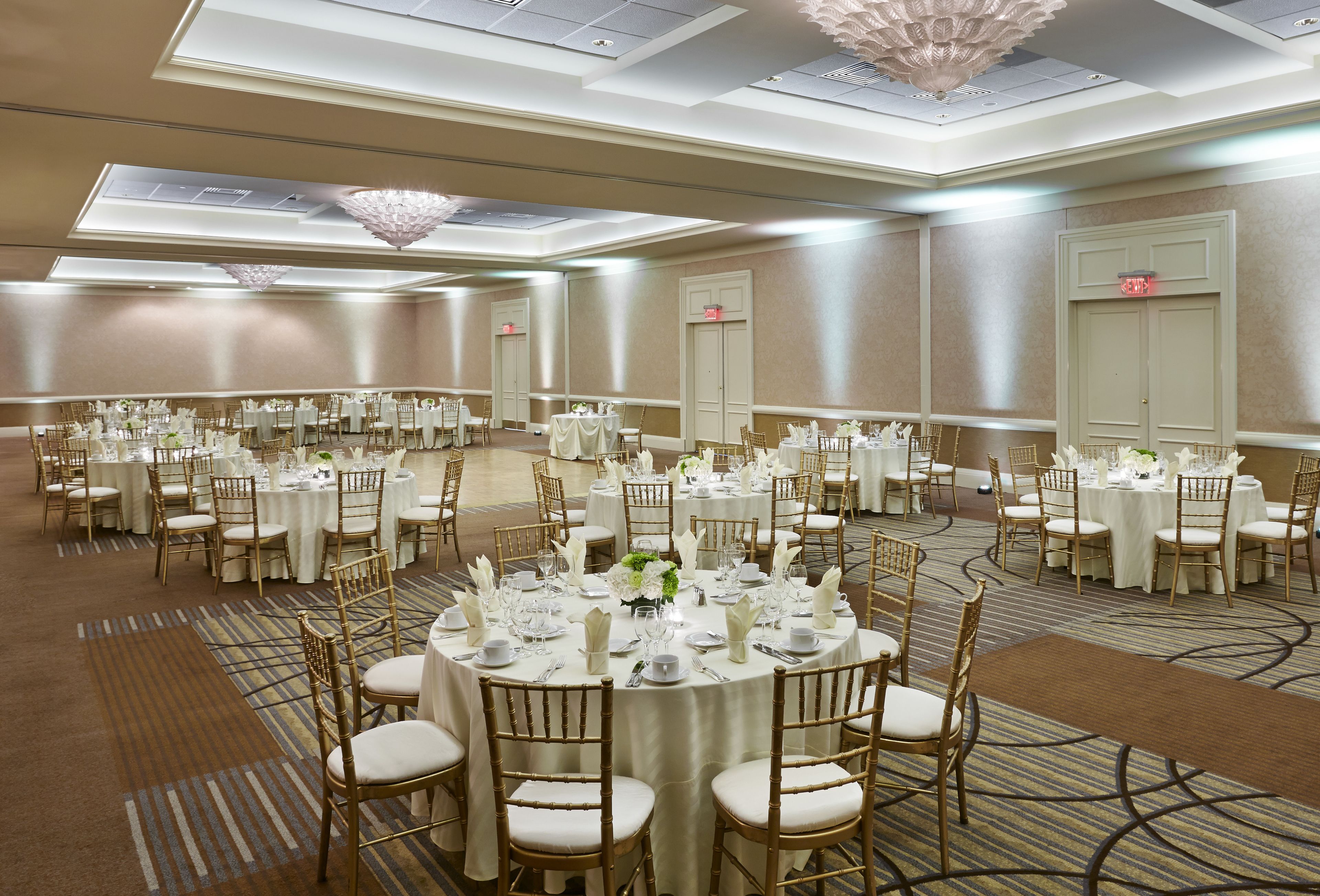 A large banquet hall with round tables set for dining, featuring gold chairs and white tablecloths.