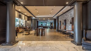 A spacious lobby with a central seating area, a bar on the left, and a wall with a clock and artwork on the right.