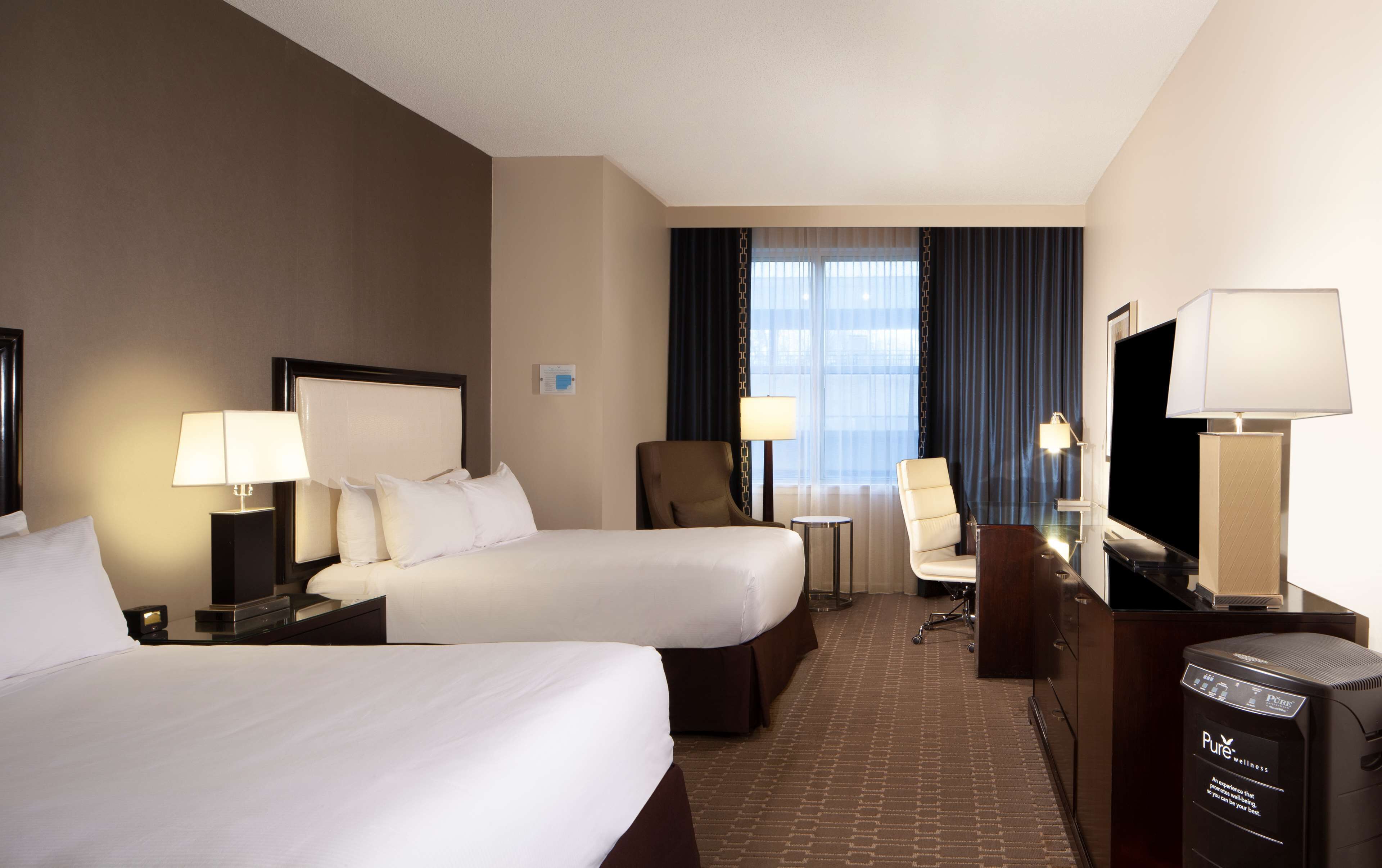 A hotel room with two beds, a desk, a chair, a TV, and a coffee maker.