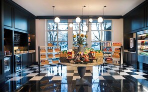 Et moderne interiør med en central udstilling af snacks og drikkevarer, store vinduer og et ternet gulv.
