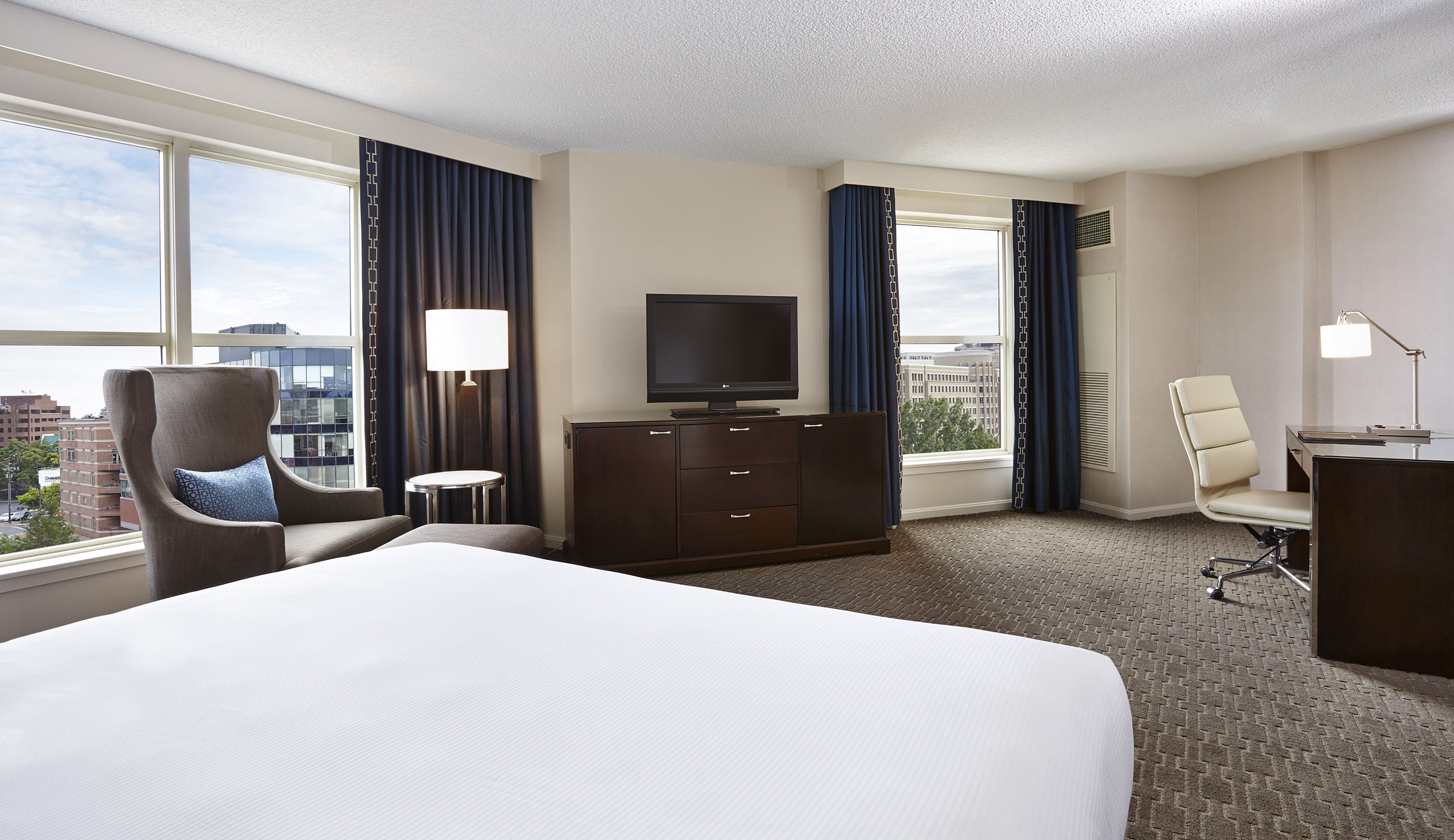Quarto de hotel com cama grande, televisão, escrivaninha, cadeira e vista para a cidade.
