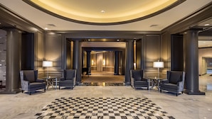 A spacious lobby with a checkered floor, two armchairs, and a grand piano.