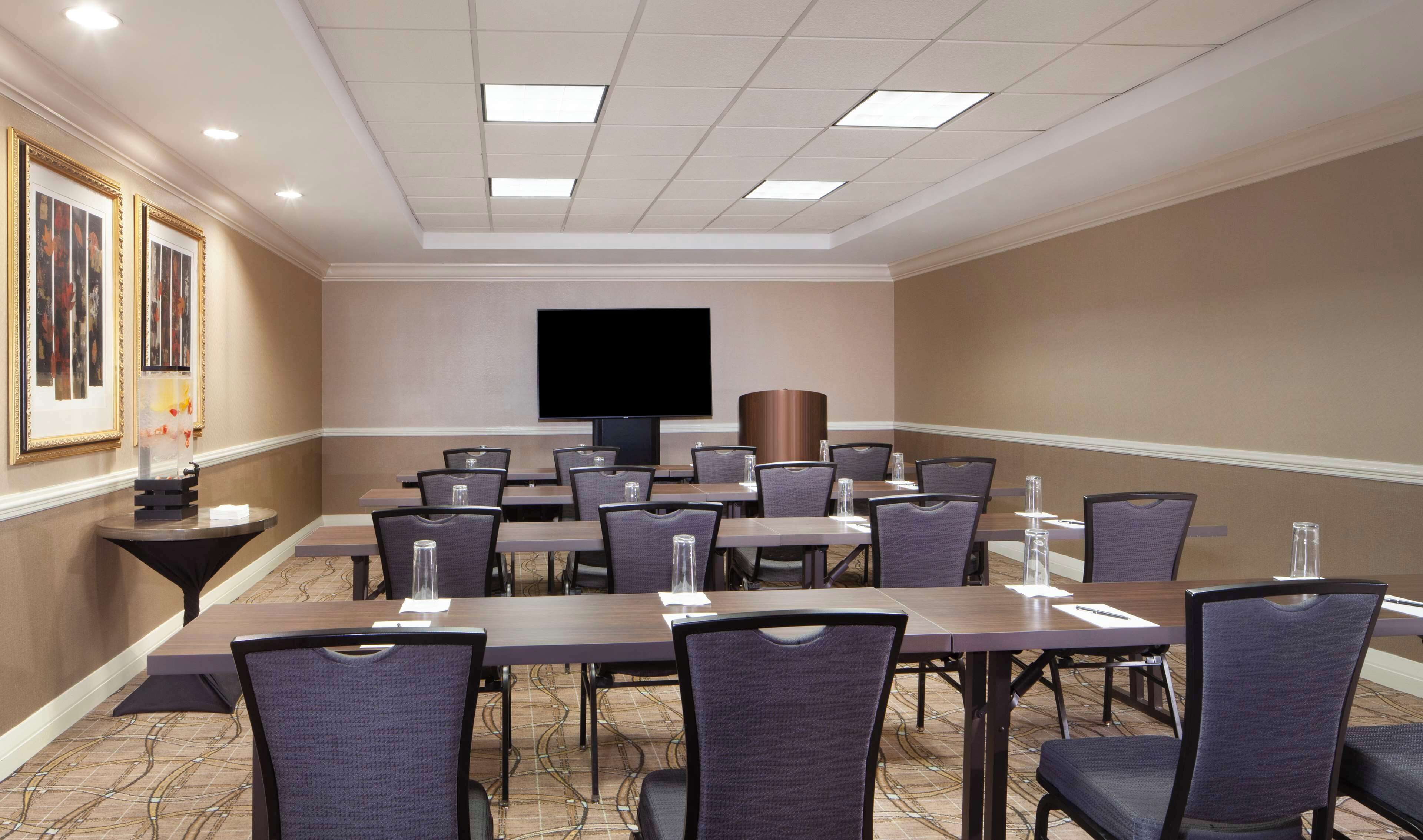 A conference room with a long table, multiple chairs, a flat-screen TV, and framed pictures on the wall.