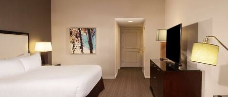 A hotel room with a large bed, a flat-screen TV, a desk, and a painting on the wall.