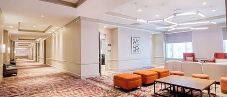 A spacious hotel lobby with a red and white patterned carpet, a seating area with orange and white chairs, and a modern ceiling design.