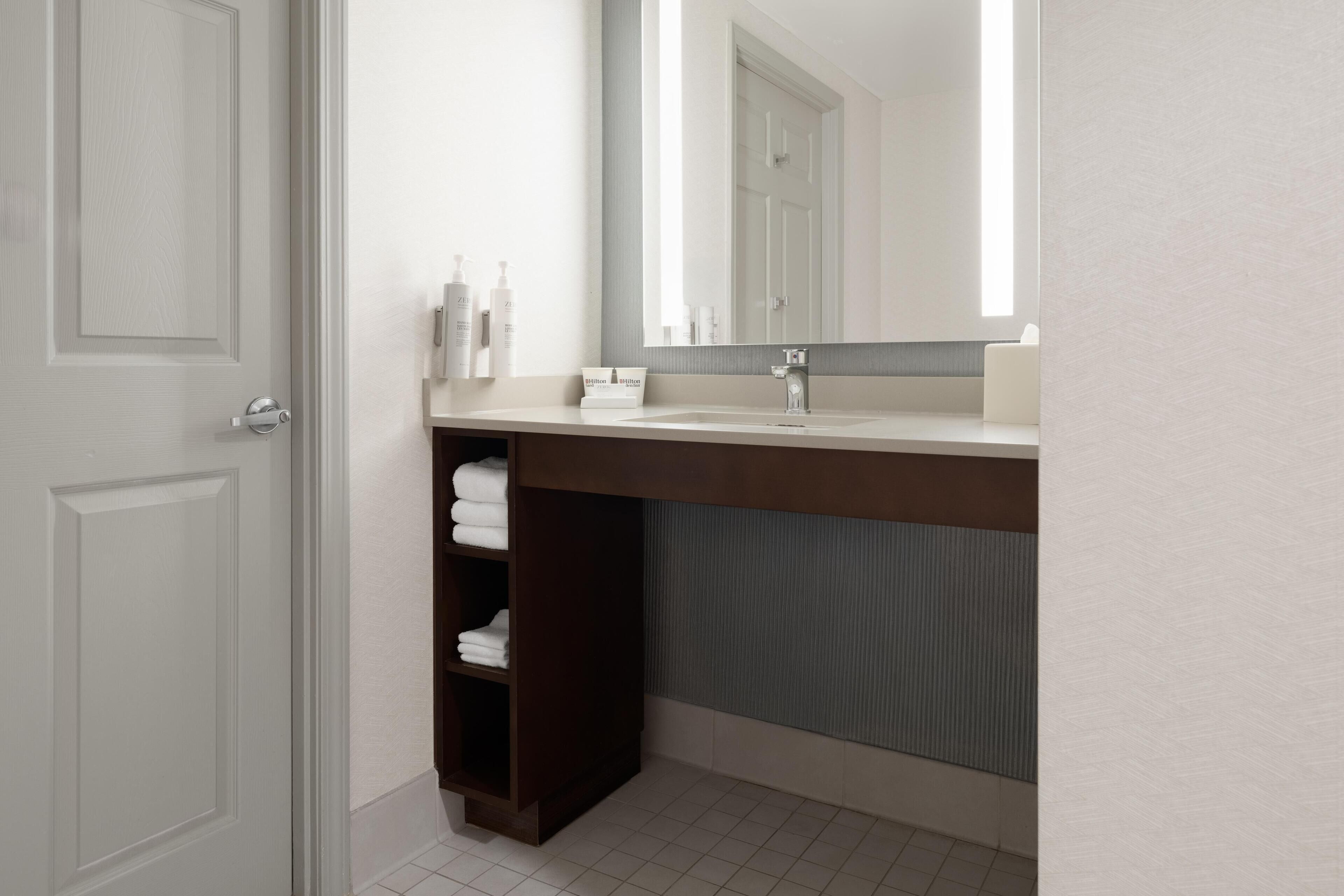 Une salle de bain avec une porte blanche, un lavabo avec un miroir et un porte-serviettes.