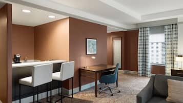 Une chambre d’hôtel équipée d’une kitchenette, d’un coin repas avec une table et des chaises, d’un canapé et d’une grande fenêtre avec des rideaux.