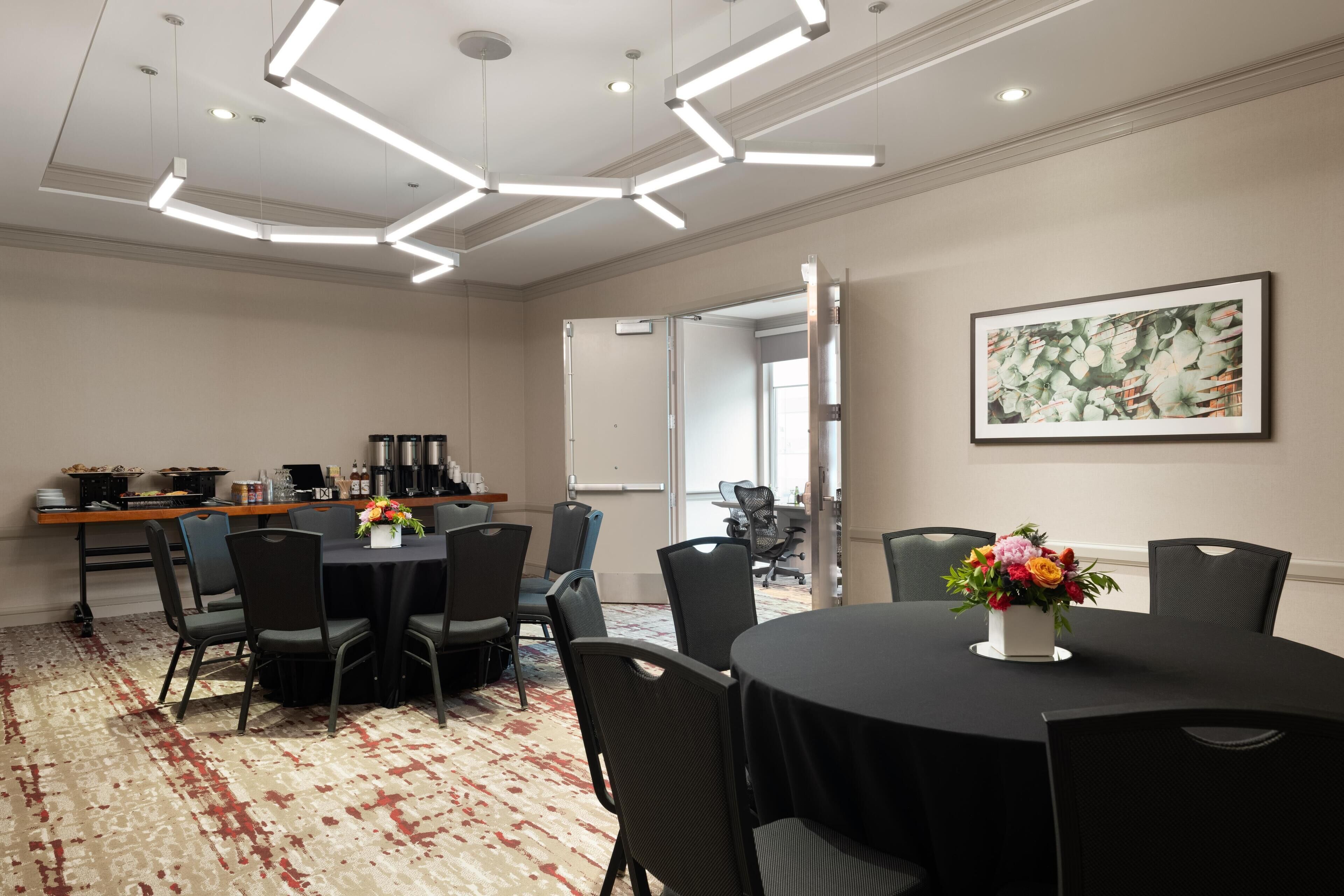 A conference room with a round table, black chairs, a floral centerpiece, and a modern ceiling light fixture.