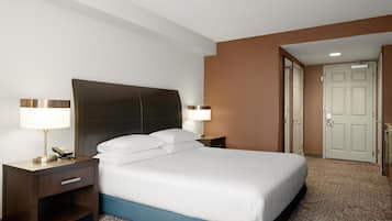 A hotel room with a large bed, two bedside tables with lamps, a nightstand with a phone, and a door leading to another room.